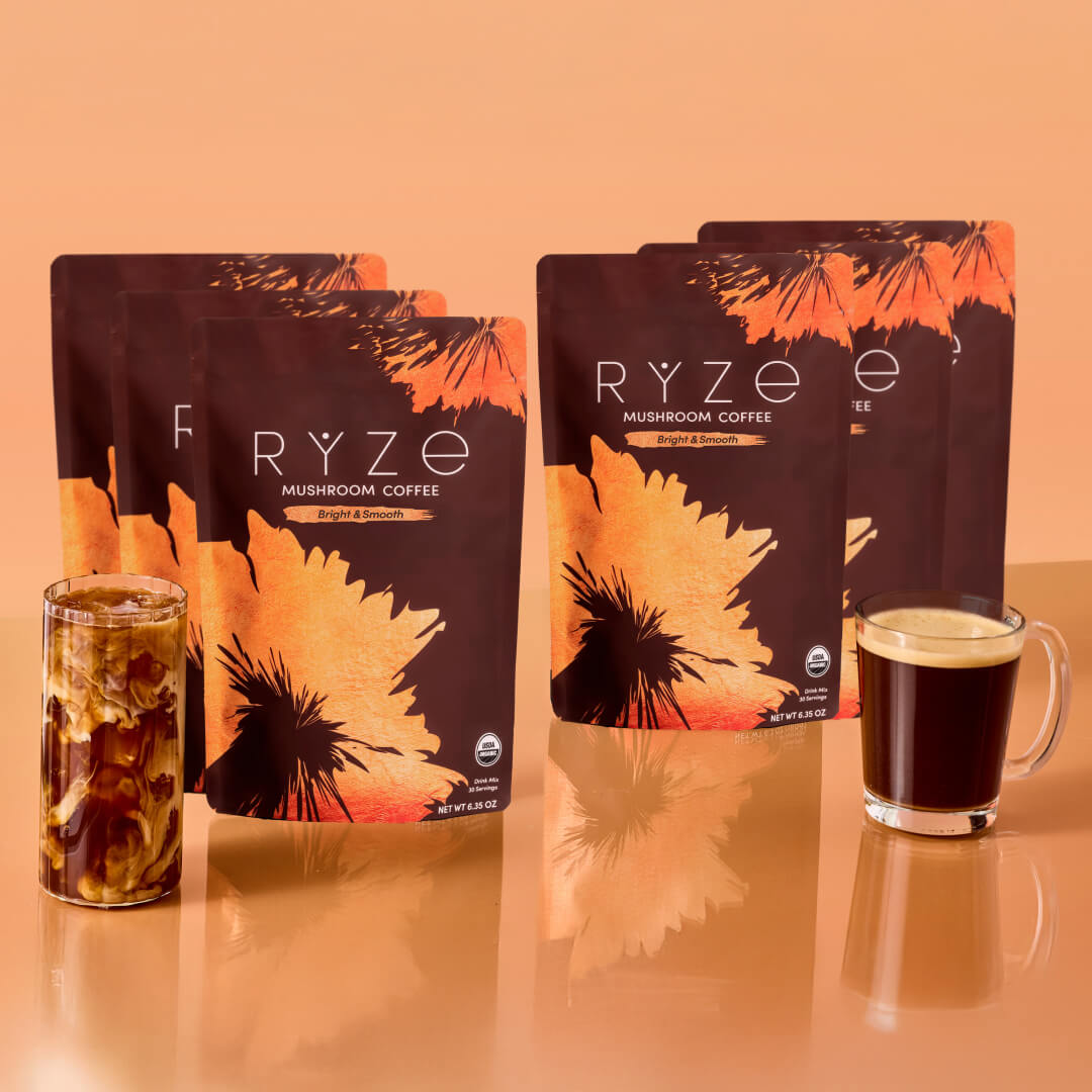 Six RYZE Mushroom Coffee Bright & Smooth bags in two groups of three, flanking iced coffee and a hot coffee glass on an...